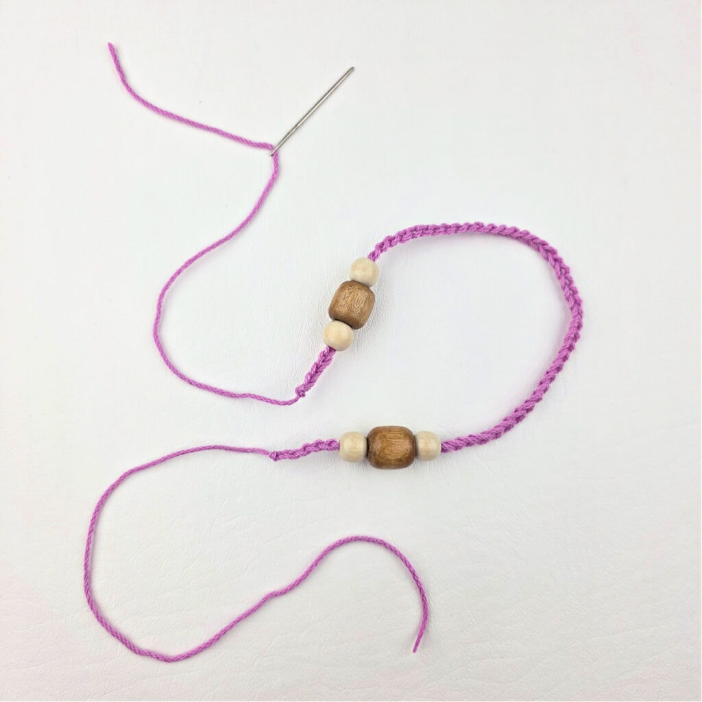 Wooden beads and a pink strand of yarn pulled through a yarn needle.