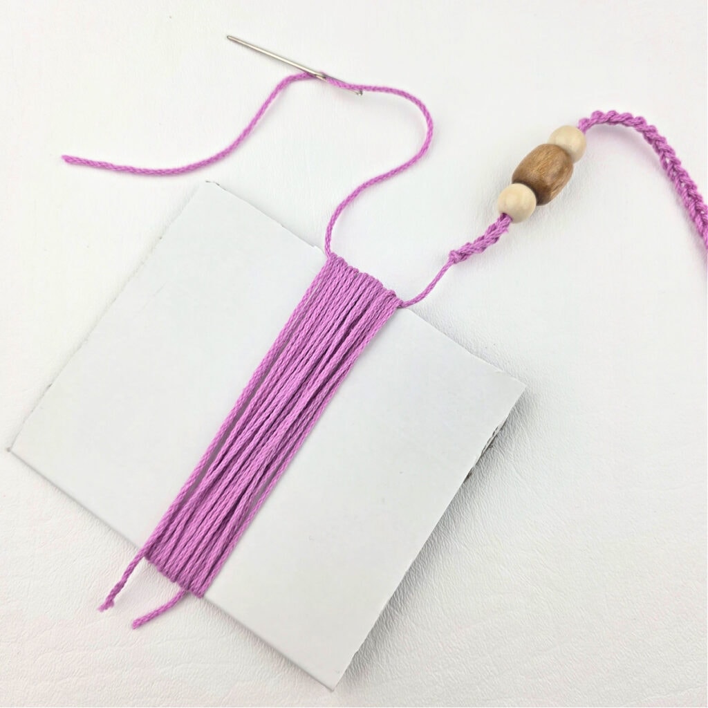 Pink yarn wrapped around a piece of paper with another piece of yarn that has wooden beads on it.