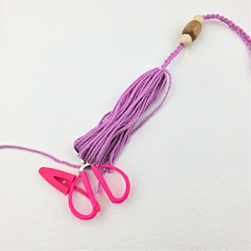 Creating a pink yarn tassel with wooden beads.