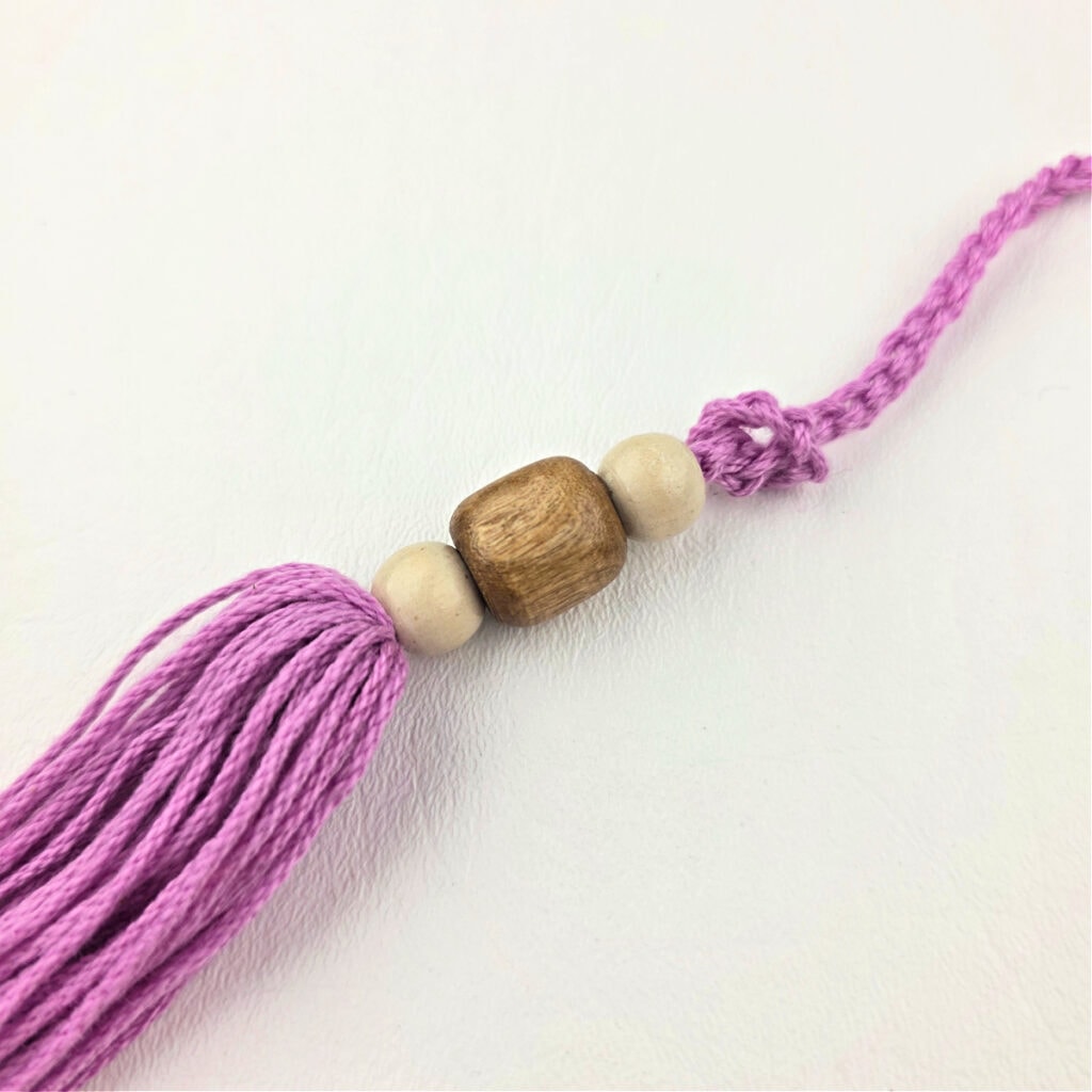 Creating a pink yarn tassel with wooden beads.