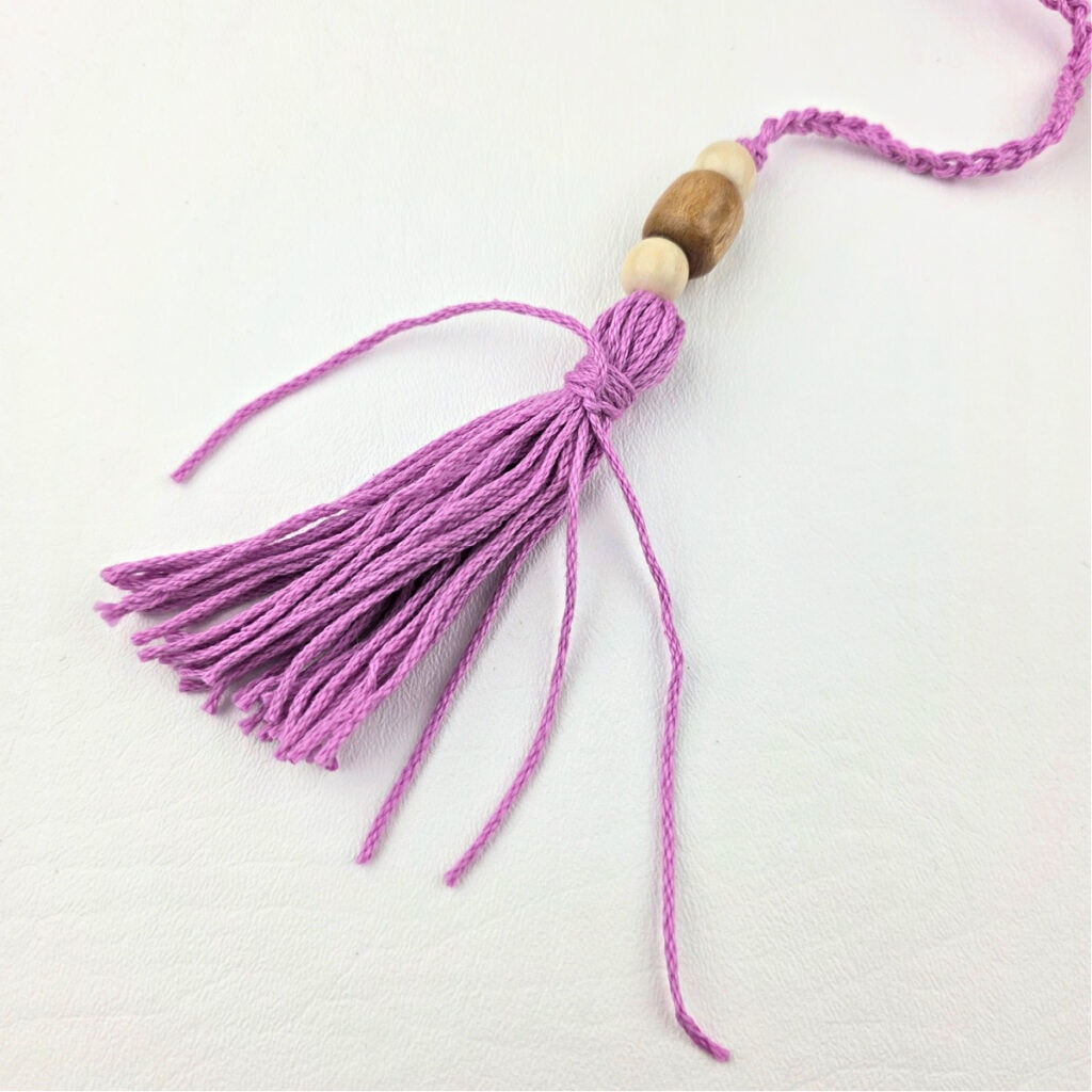 Creating a pink yarn tassel with wooden beads.