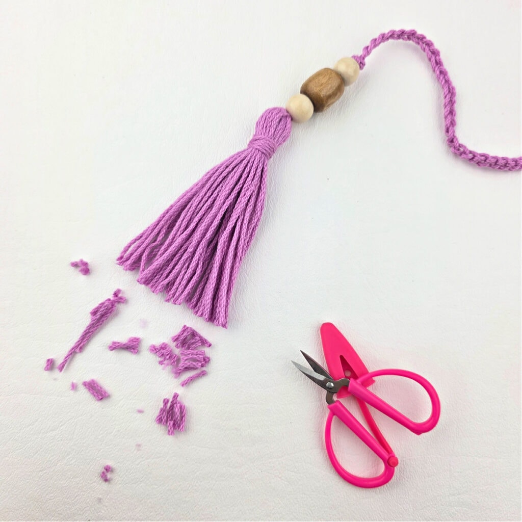 Creating a pink yarn tassel with wooden beads by trimming the uneven edges of the tassel.