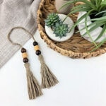 Two handmade yarn tassels with beads next to a basket of potted plants.