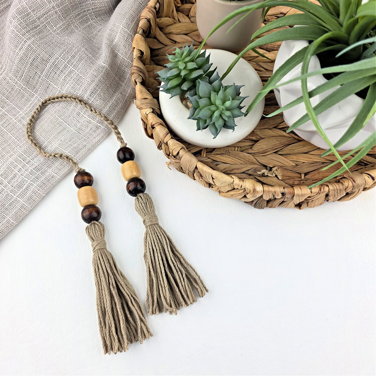 Two handmade yarn tassels with beads next to a basket of potted plants.