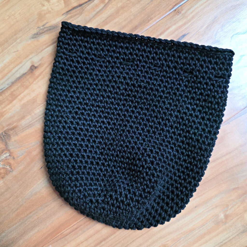The body of a crochet black cat treat bag on a wooden background.