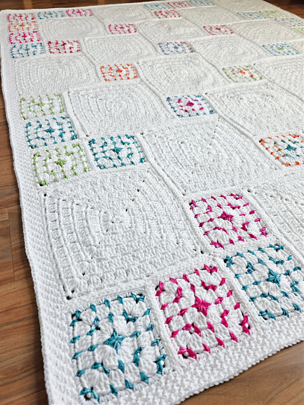 White crochet blanket with colorful squares spread out over the wooden floor.