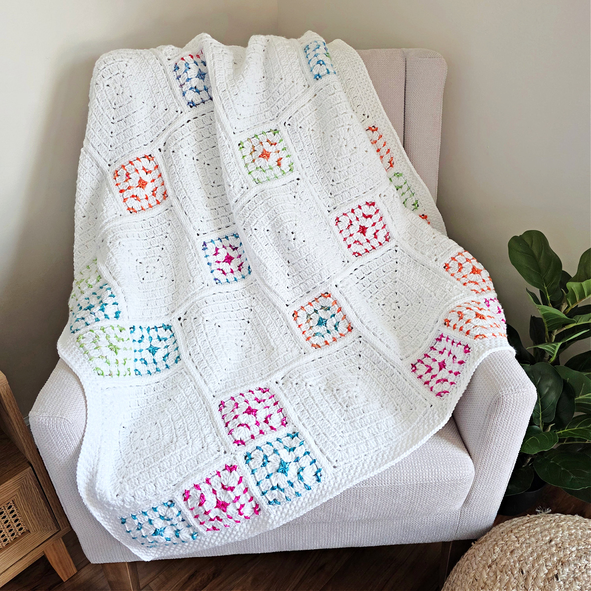 White crochet blanket with colorful squares spread out over a sofa.