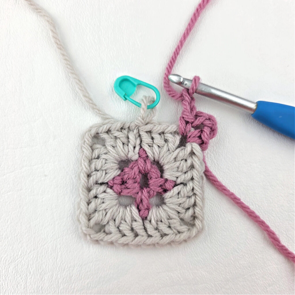 Making a block stitch granny square with a blue crochet hook and stitch marker.