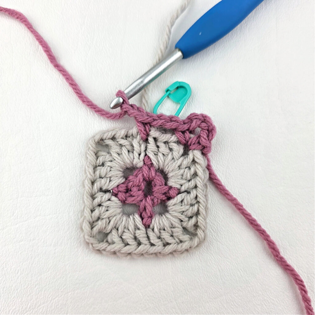 Making a block stitch granny square with a blue crochet hook and stitch marker.