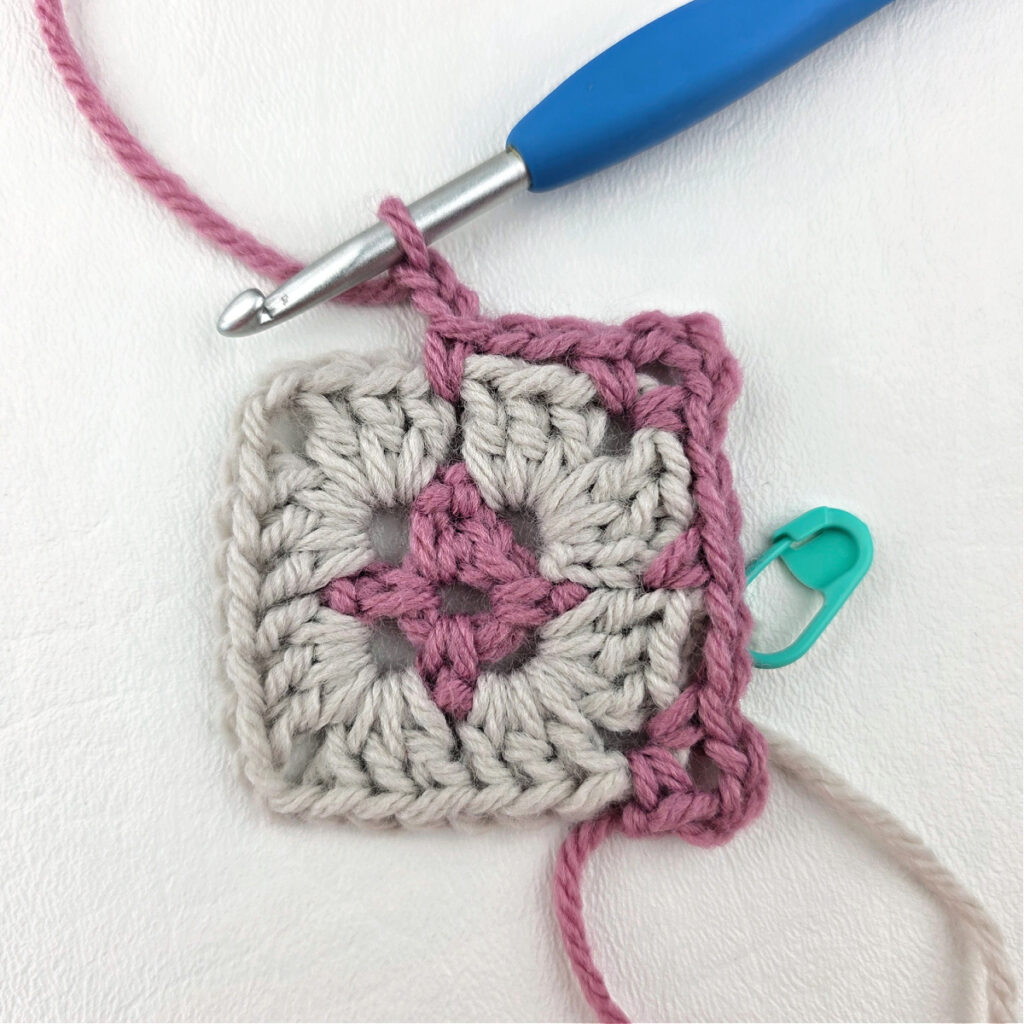 Making a block stitch granny square with a blue crochet hook and stitch marker.