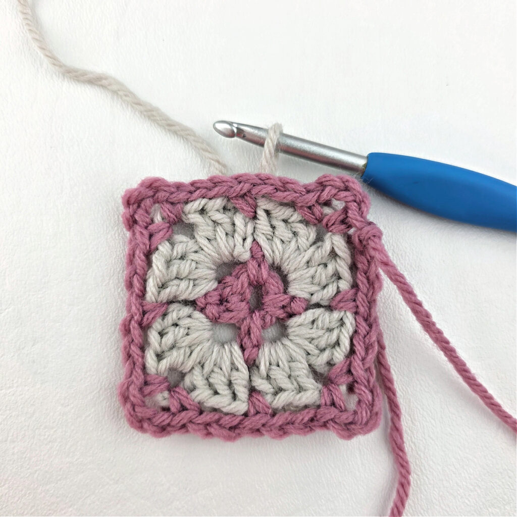 Making a block stitch granny square with a blue crochet hook.