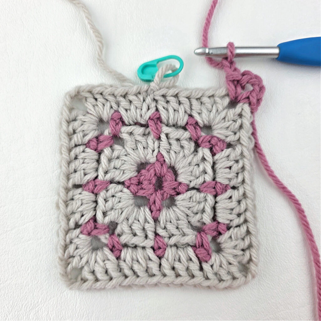 Making a block stitch granny square with a blue crochet hook.