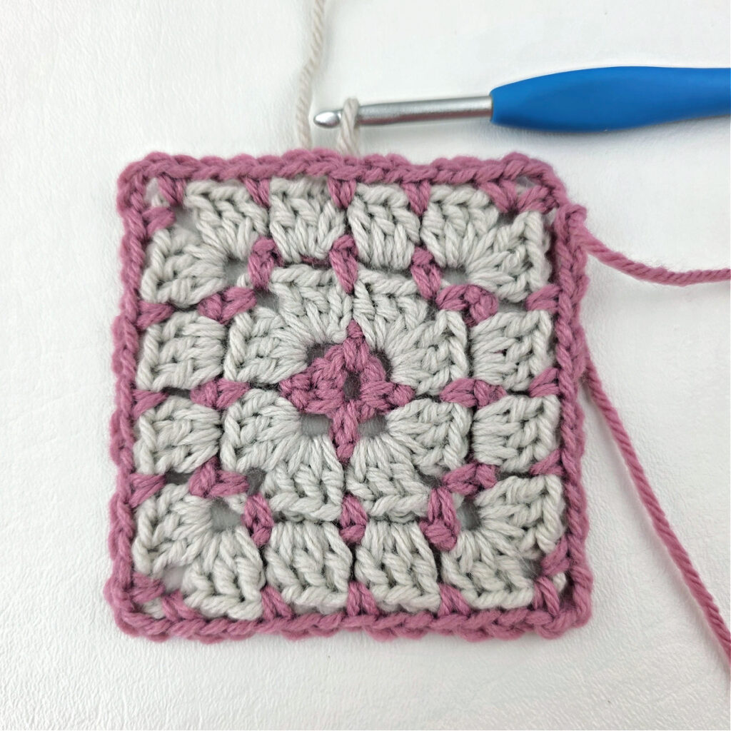 Making a block stitch granny square with a blue crochet hook.