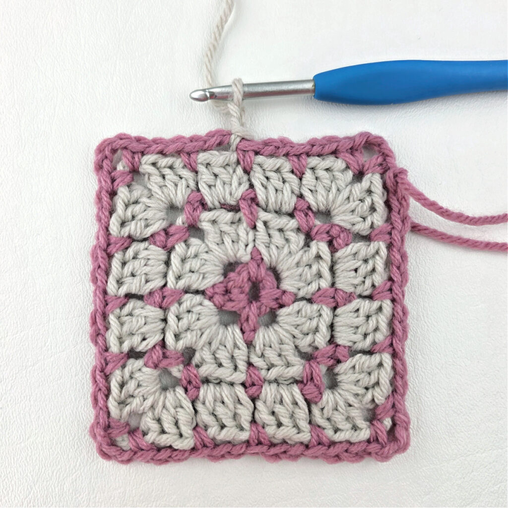 Making a block stitch granny square with a blue crochet hook.