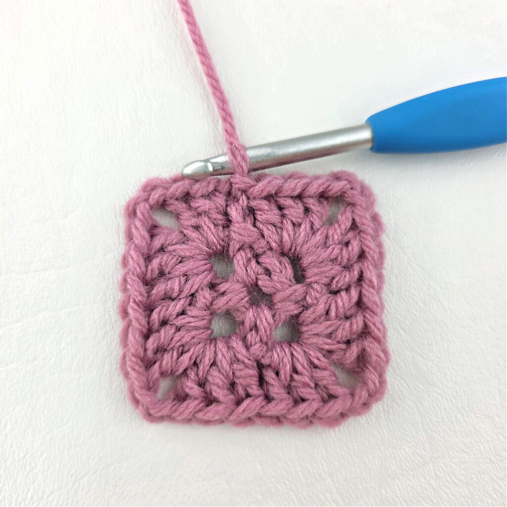 Making a block stitch granny square with a blue crochet hook.