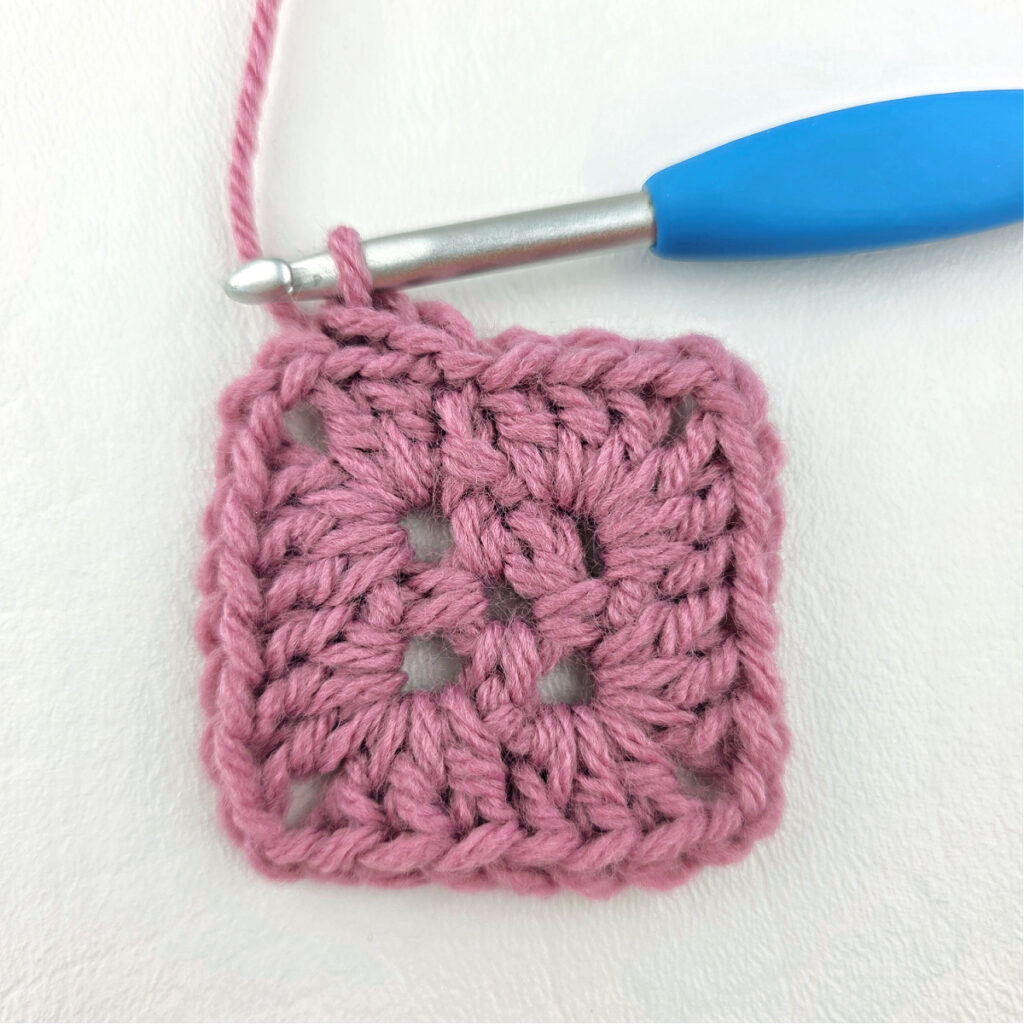 Making a block stitch granny square with a blue crochet hook.