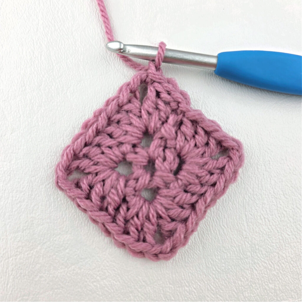 Making a block stitch granny square with a blue crochet hook.