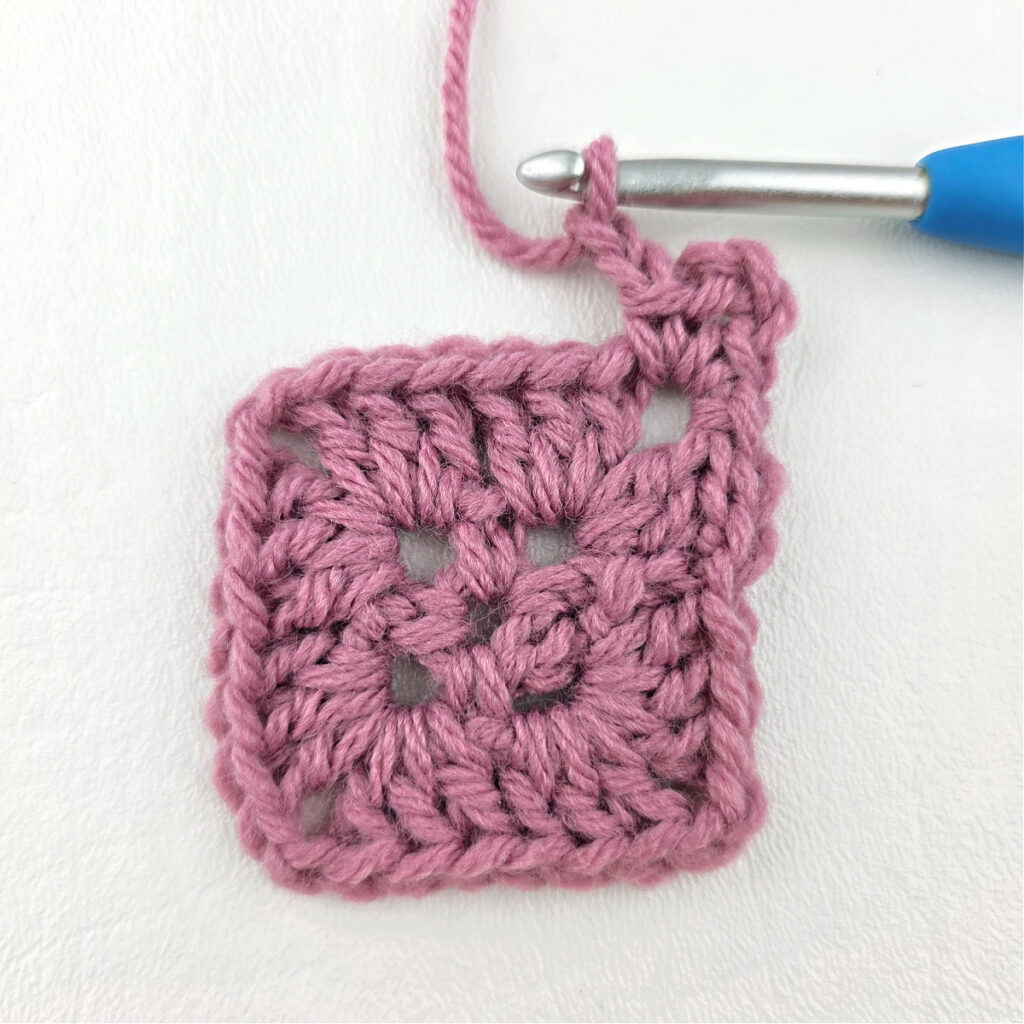 Making a block stitch granny square with a blue crochet hook.