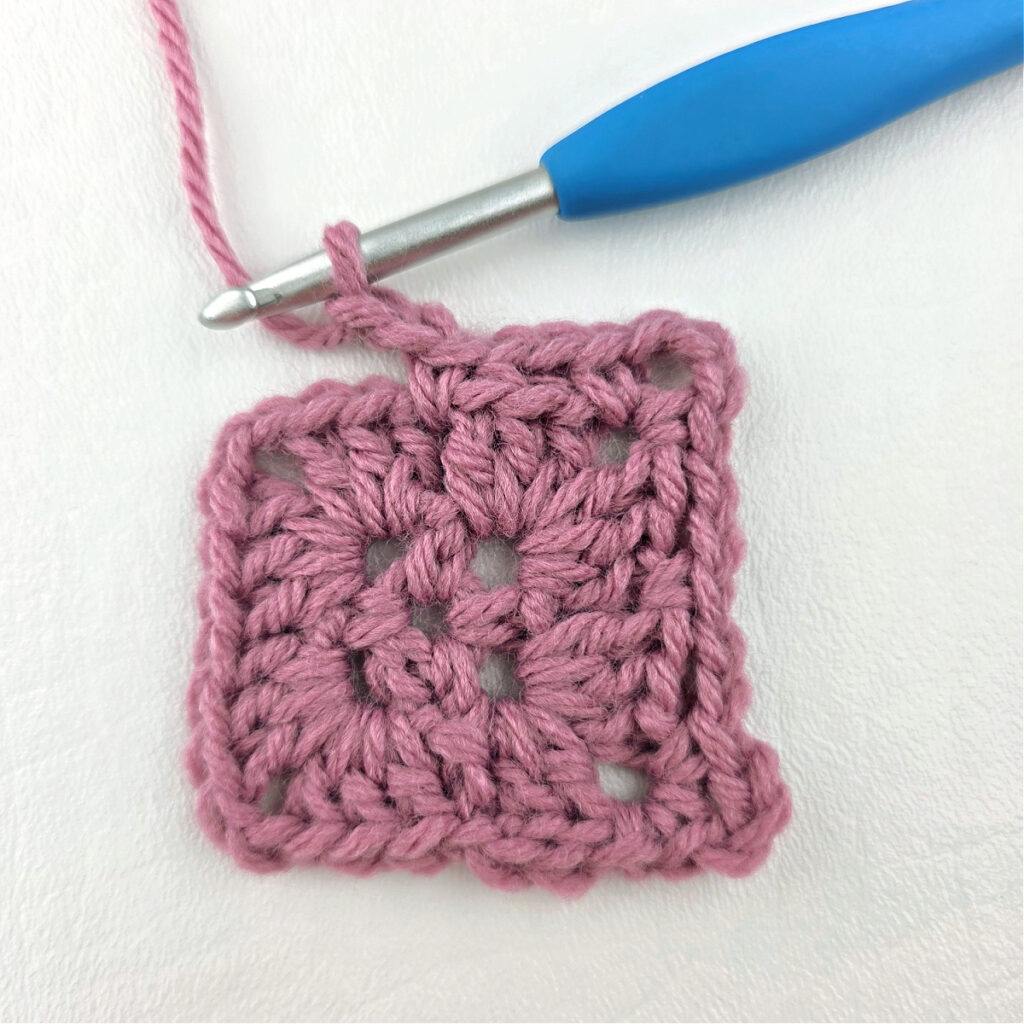 Making a block stitch granny square with a blue crochet hook.