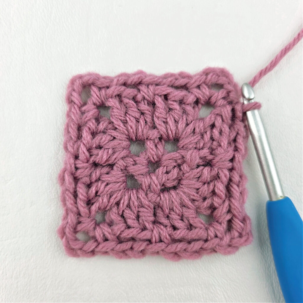 Making a block stitch granny square with a blue crochet hook.