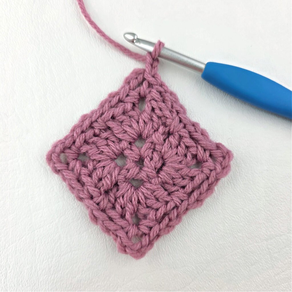 Making a block stitch granny square with a blue crochet hook.