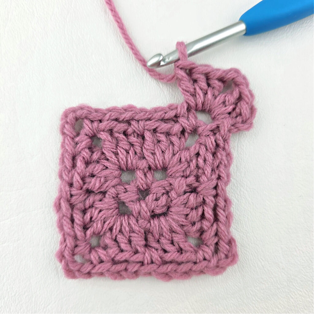 Making a block stitch granny square with a blue crochet hook.