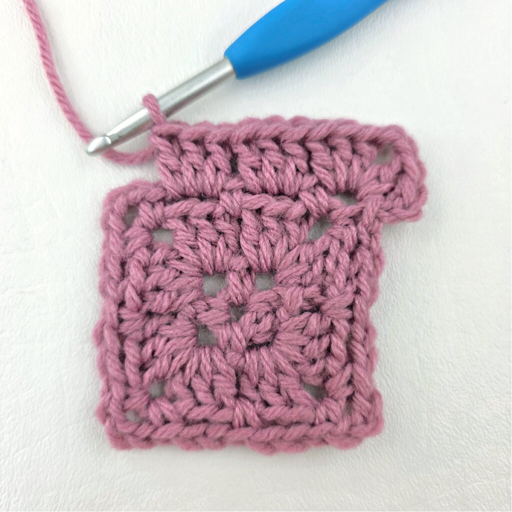 Making a block stitch granny square with a blue crochet hook.