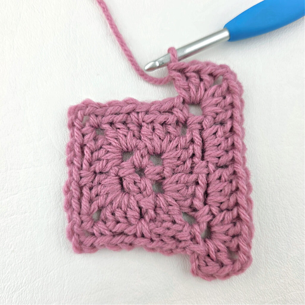 Making a block stitch granny square with a blue crochet hook.