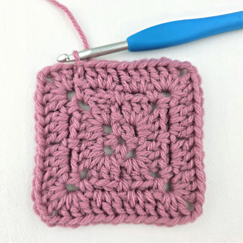 Making a block stitch granny square with a blue crochet hook.