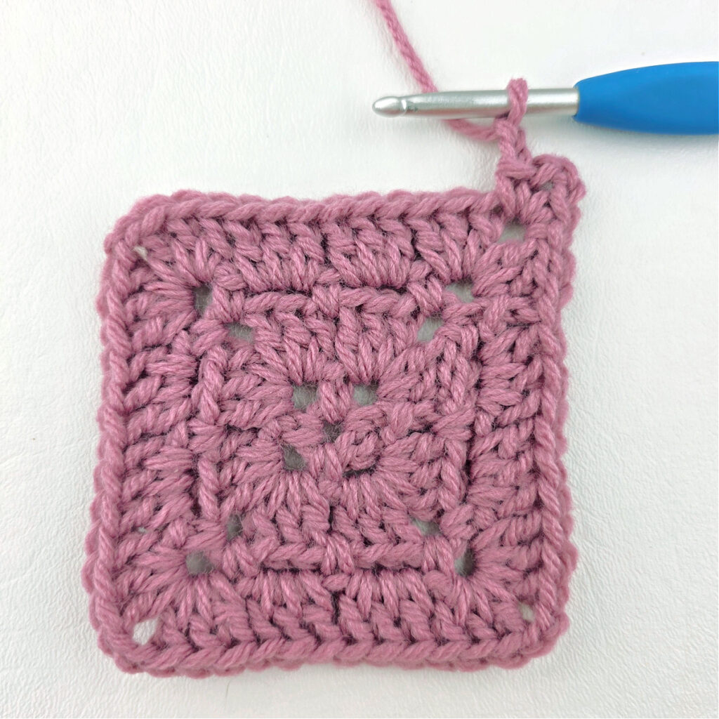 Making a block stitch granny square with a blue crochet hook.