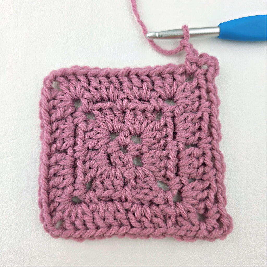 Making a block stitch granny square with a blue crochet hook.