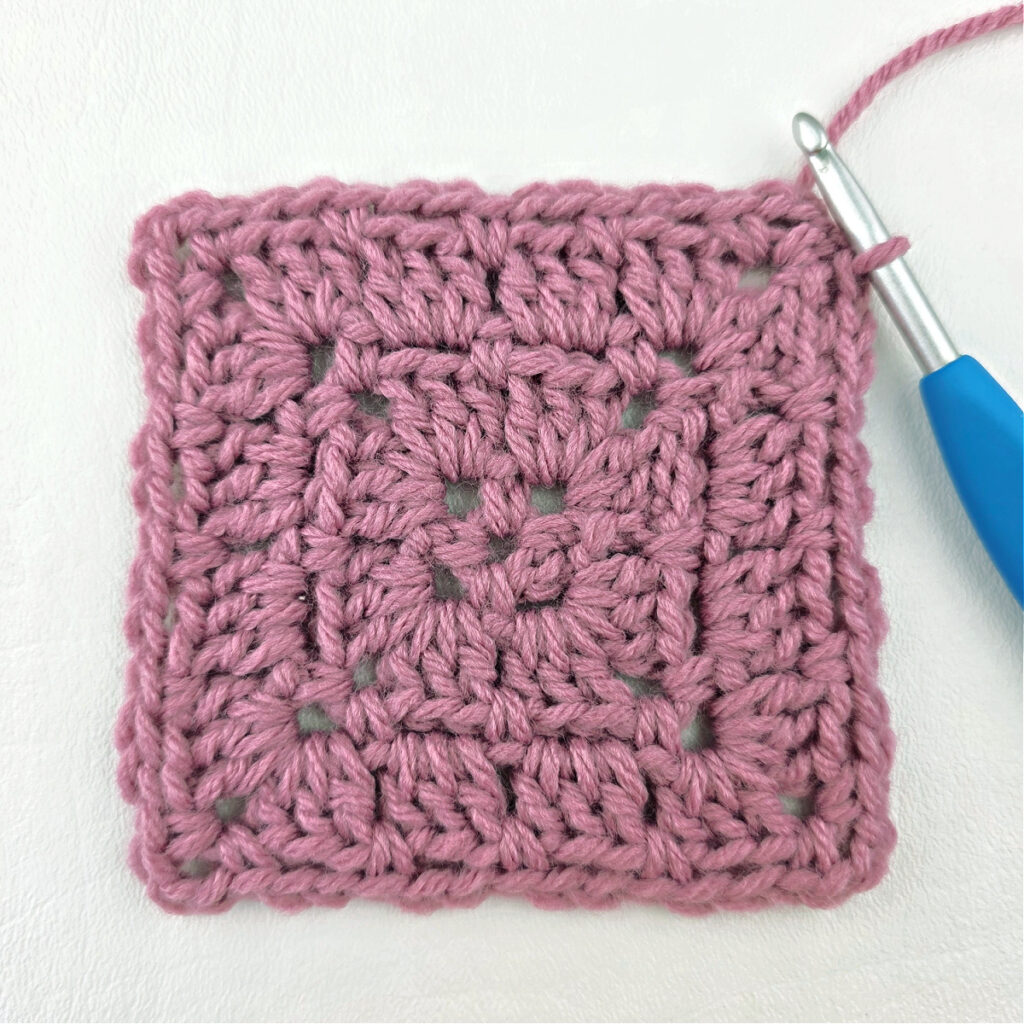 Making a block stitch granny square with a blue crochet hook.
