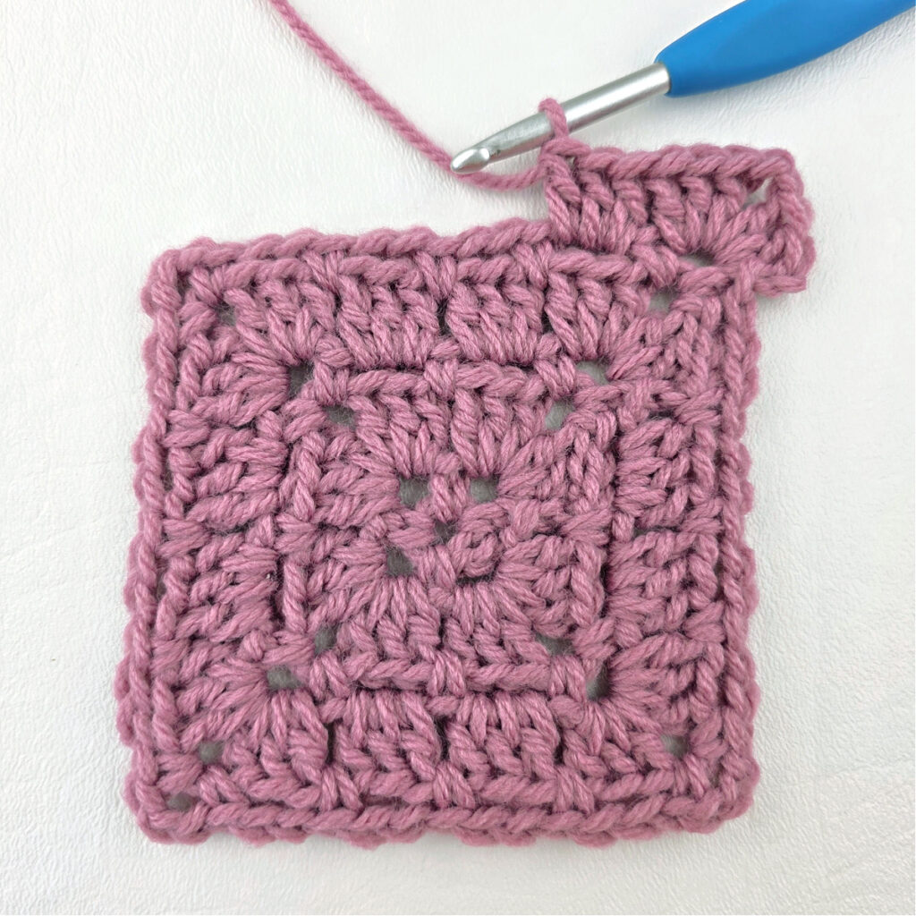 Making a block stitch granny square with a blue crochet hook.
