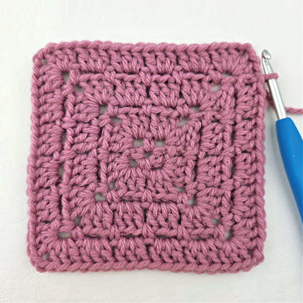 Making a block stitch granny square with a blue crochet hook.