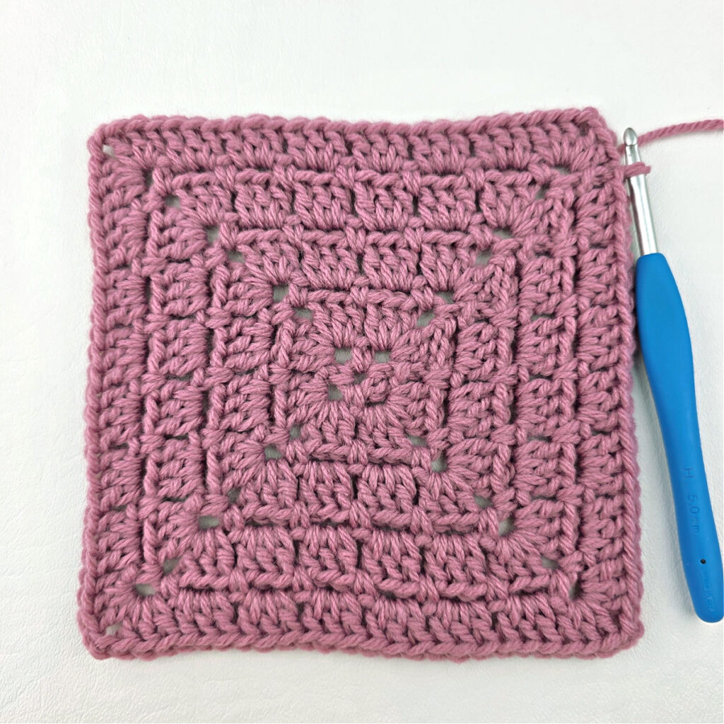 Making a block stitch granny square with a blue crochet hook.