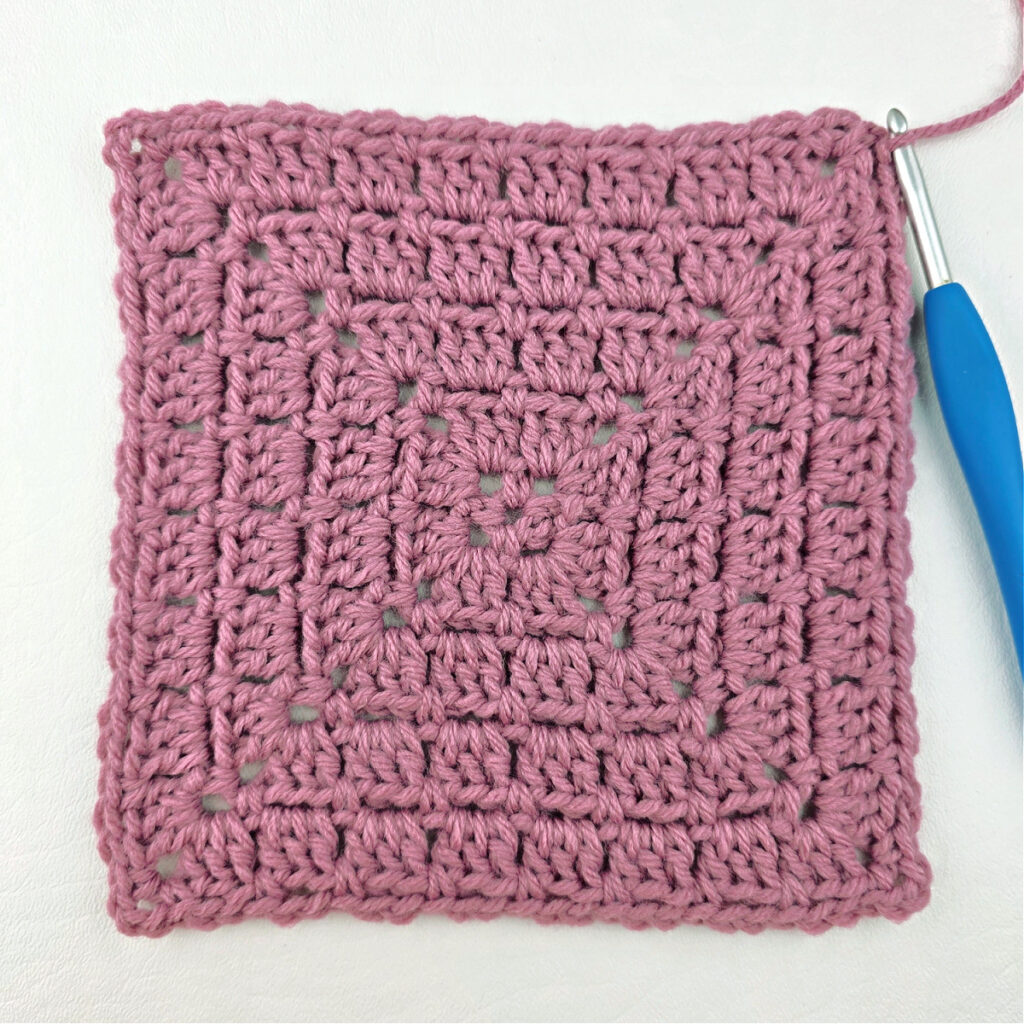 Making a block stitch granny square with a blue crochet hook.