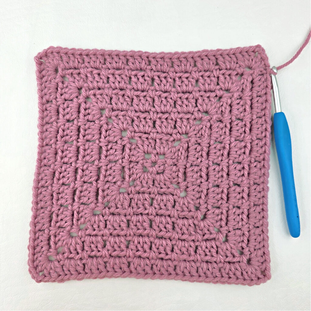 Making a block stitch granny square with a blue crochet hook.