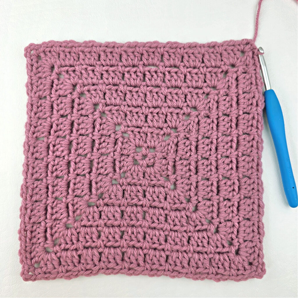 Making a block stitch granny square with a blue crochet hook.