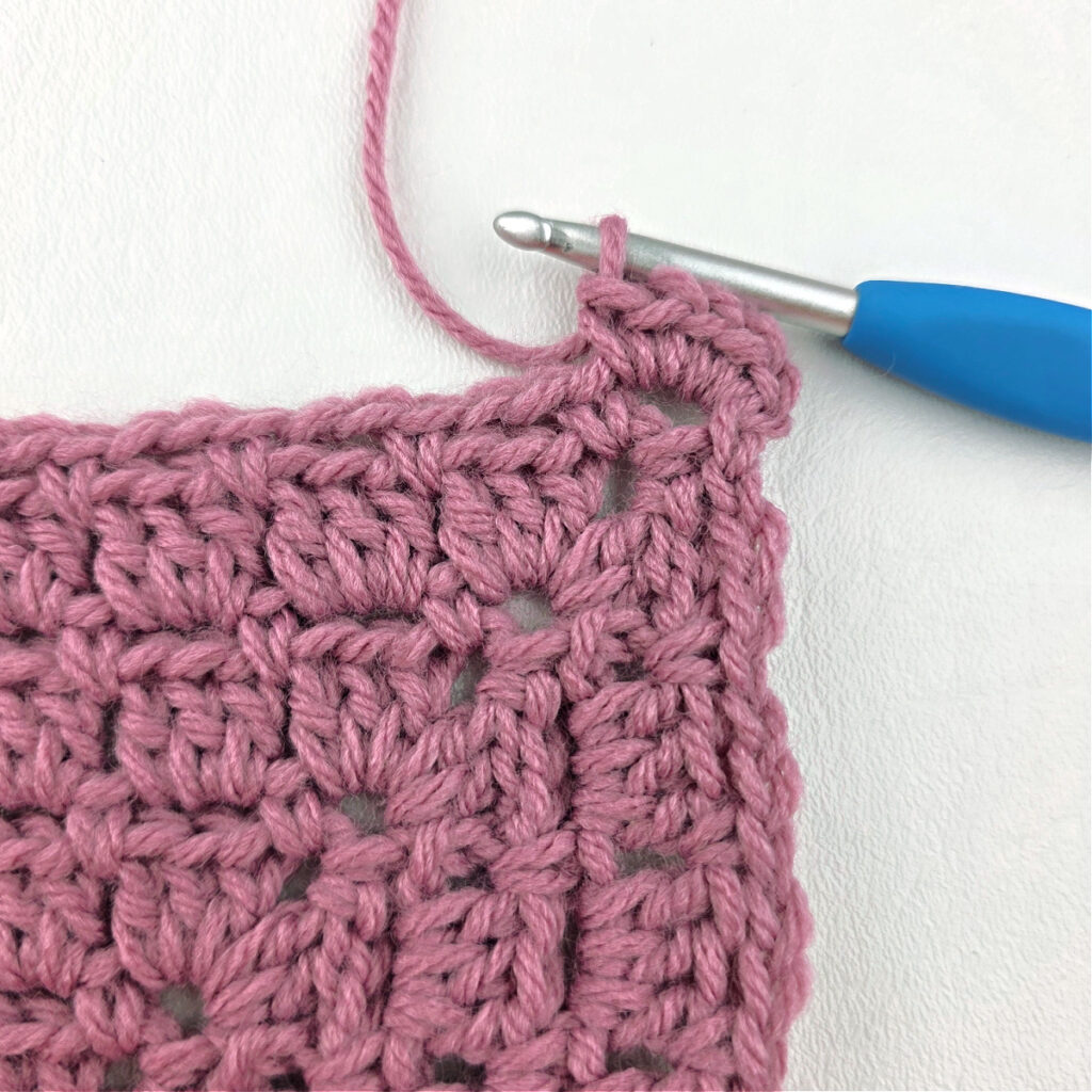 Making a block stitch granny square with a blue crochet hook.