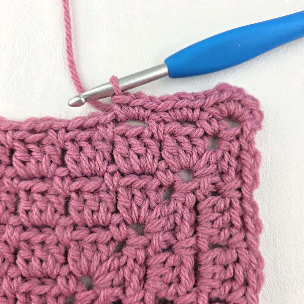Making a block stitch granny square with a blue crochet hook.