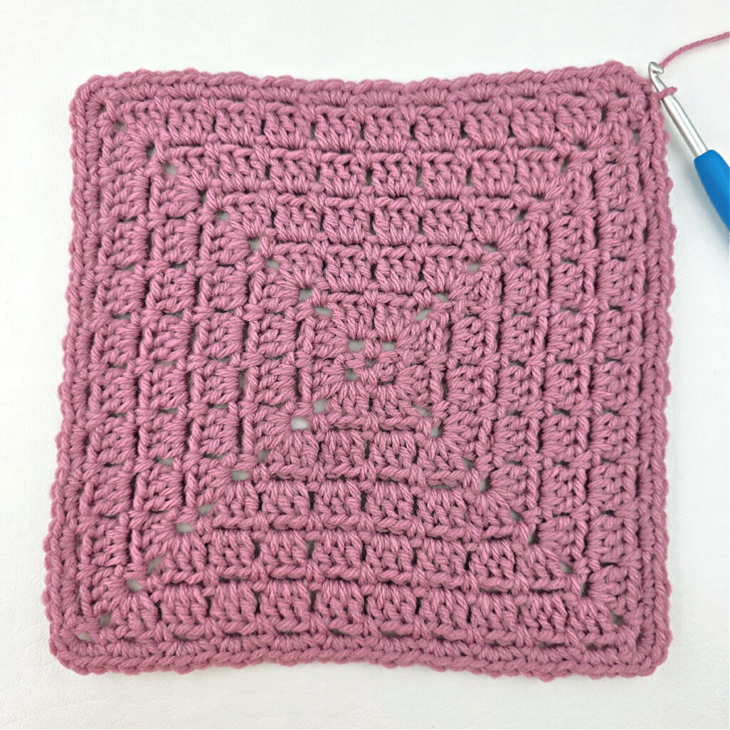 Making a block stitch granny square with a blue crochet hook.