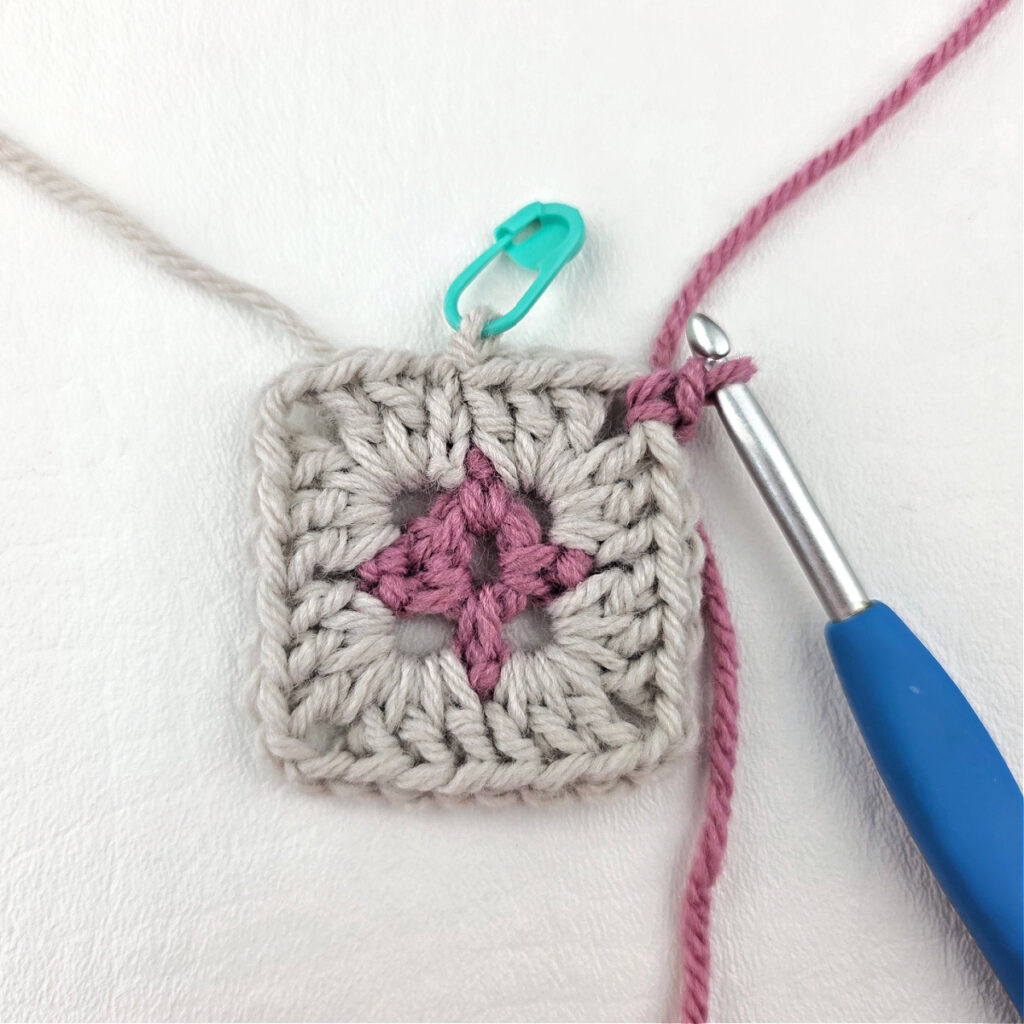 Making a block stitch granny square with a blue crochet hook and stitch marker.