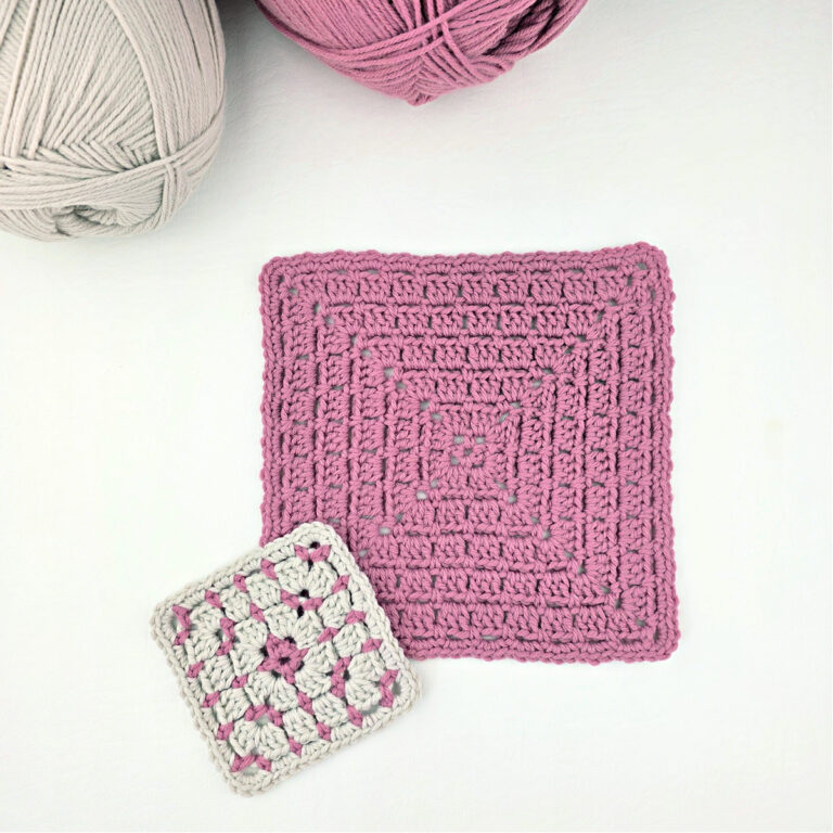 One large pink block stitch granny square and one small white and pink granny square with two balls of yarn in the corner.