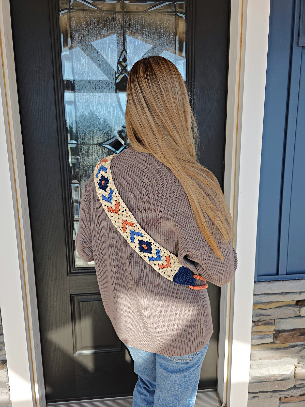 Girl in a brown pullover with a boho crochet sling bag strap over her shoulder standing with her back to the camera.