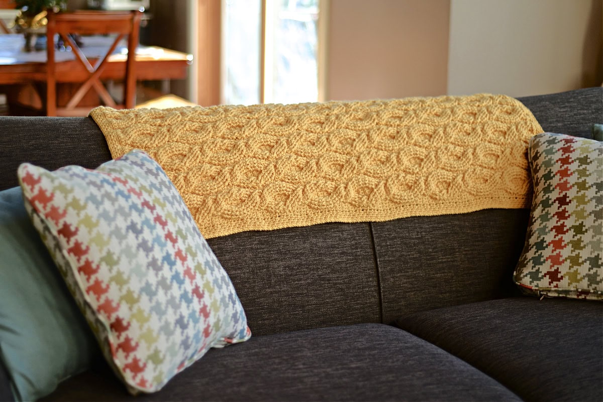 Yellow crochet blanket draped over a sofa with colorful cushions.
