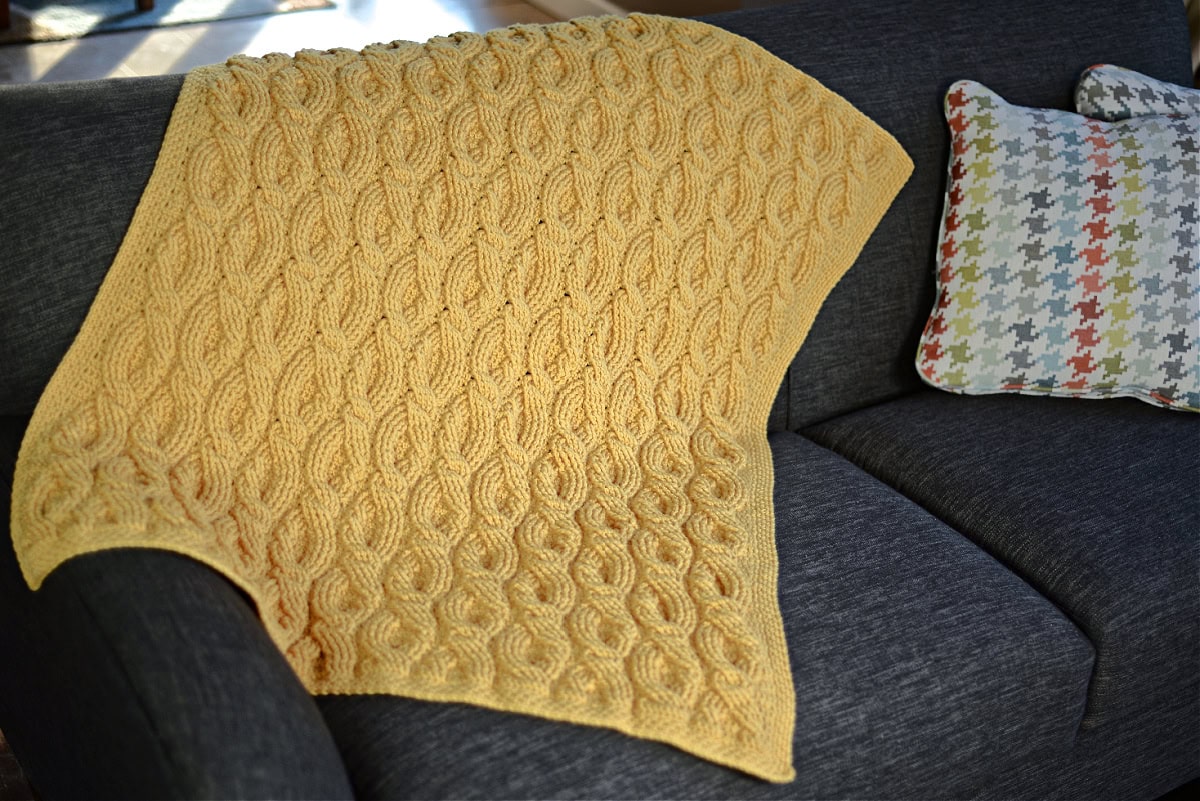 Yellow crochet blanket draped over a sofa with colorful cushions.