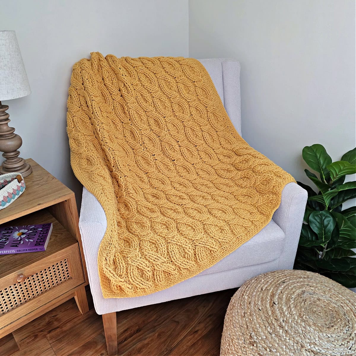 Yellow crochet blanket draped over a sofa chair with a plant next to it.