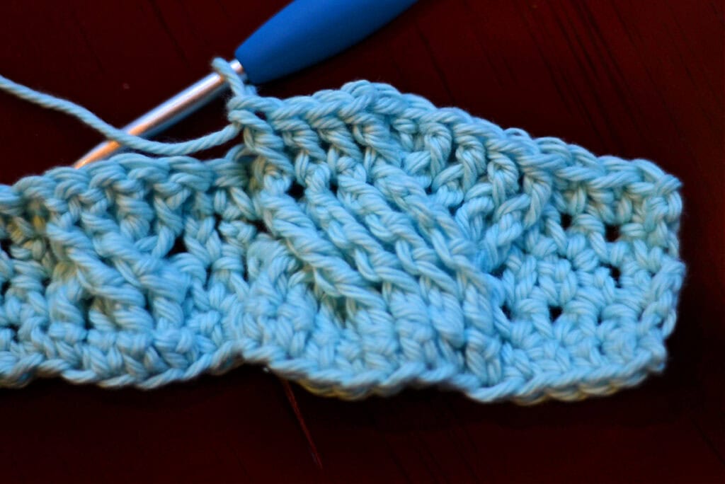 Creating crochet cables with a blue crochet hook.