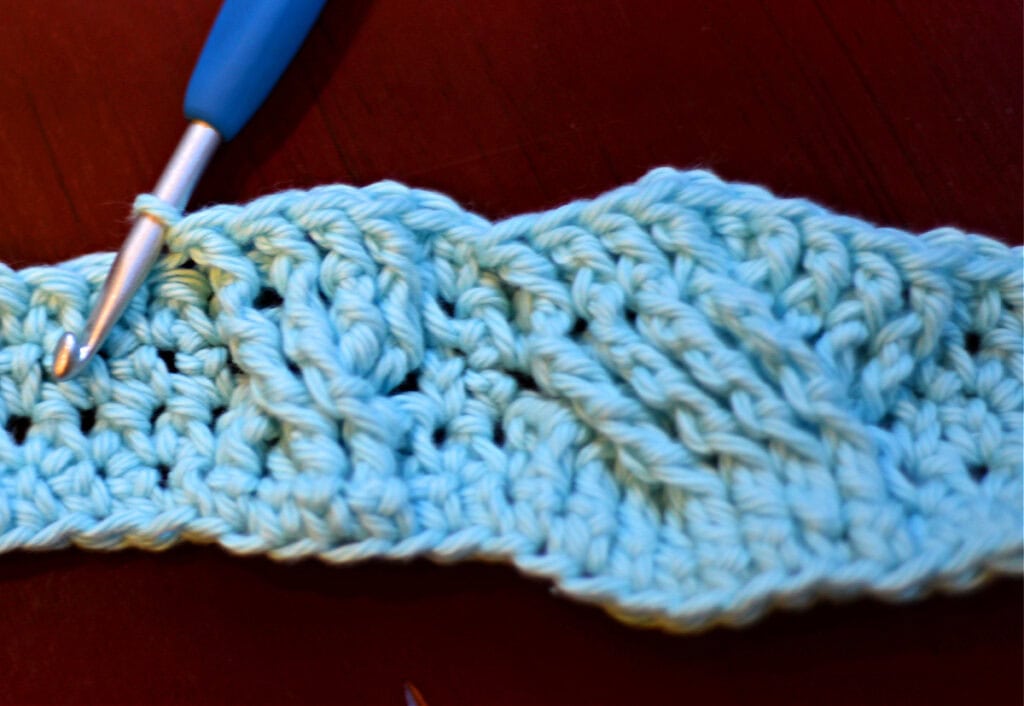 Creating crochet cables with a blue crochet hook.