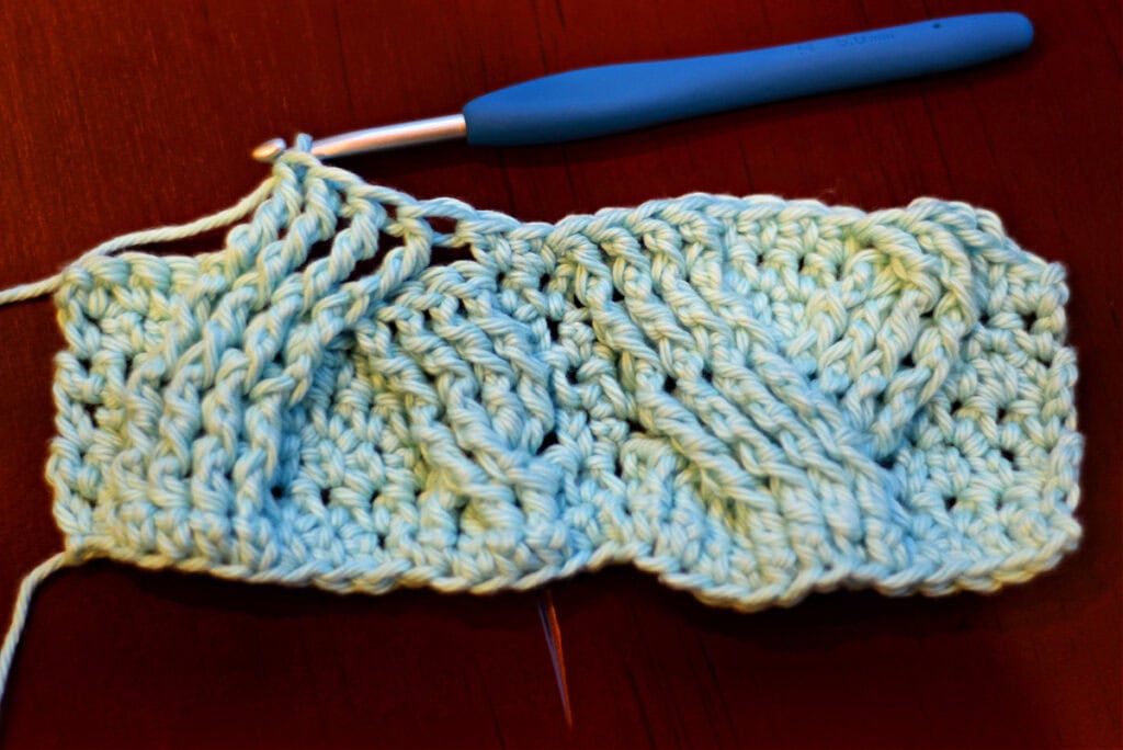 Creating crochet cables with a blue crochet hook.